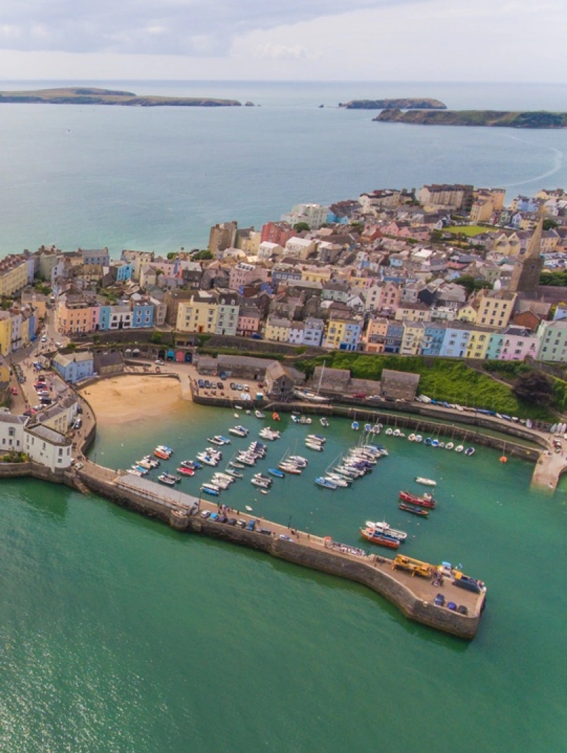 An aerial shot of a pretty harbour town with beaches, a castle, harbour and lifeboat station.