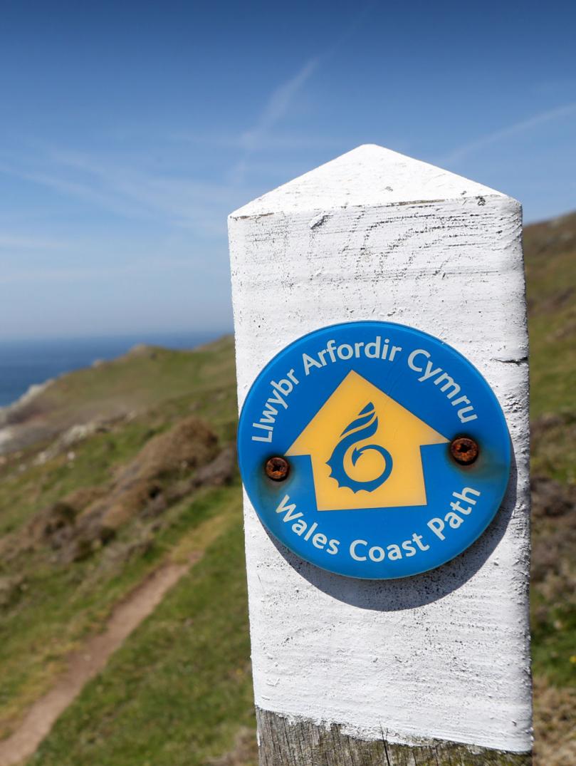 Signpost on coastal path looking over water.