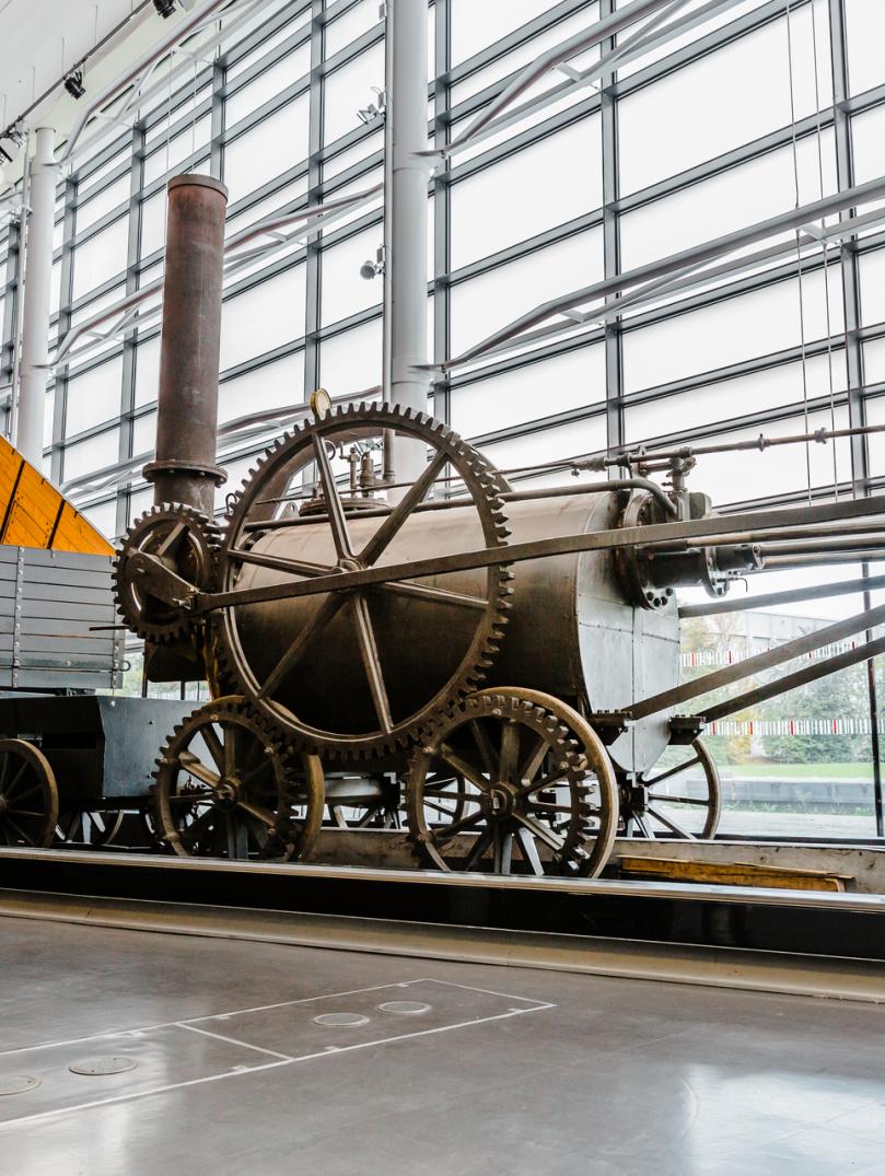 An industrial steam engine and wagon displayed in a window fronted museum.