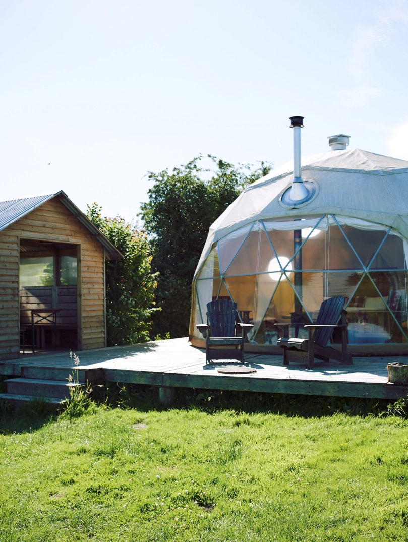  Image of a dome tent and a small hut in a field.