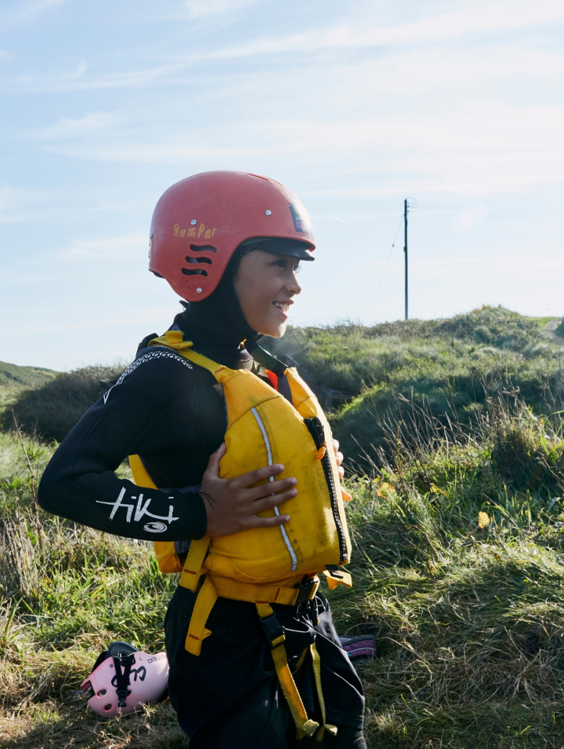 A boy in a yellow life-jacket and red helmet waiting to coasteer in Abereiddy, Pembrokeshire.