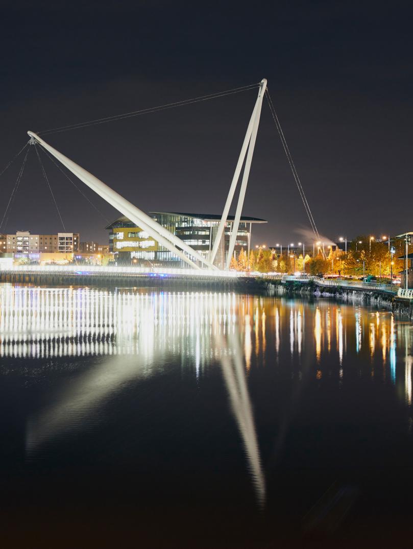 Newport city footbridge at night with lights reflecting in the water.