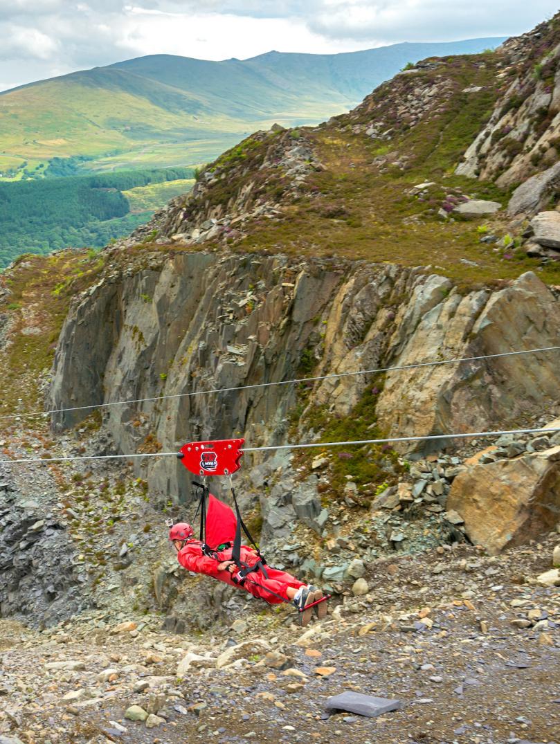 A man strapped into a zipwire travelling down it into a quarry