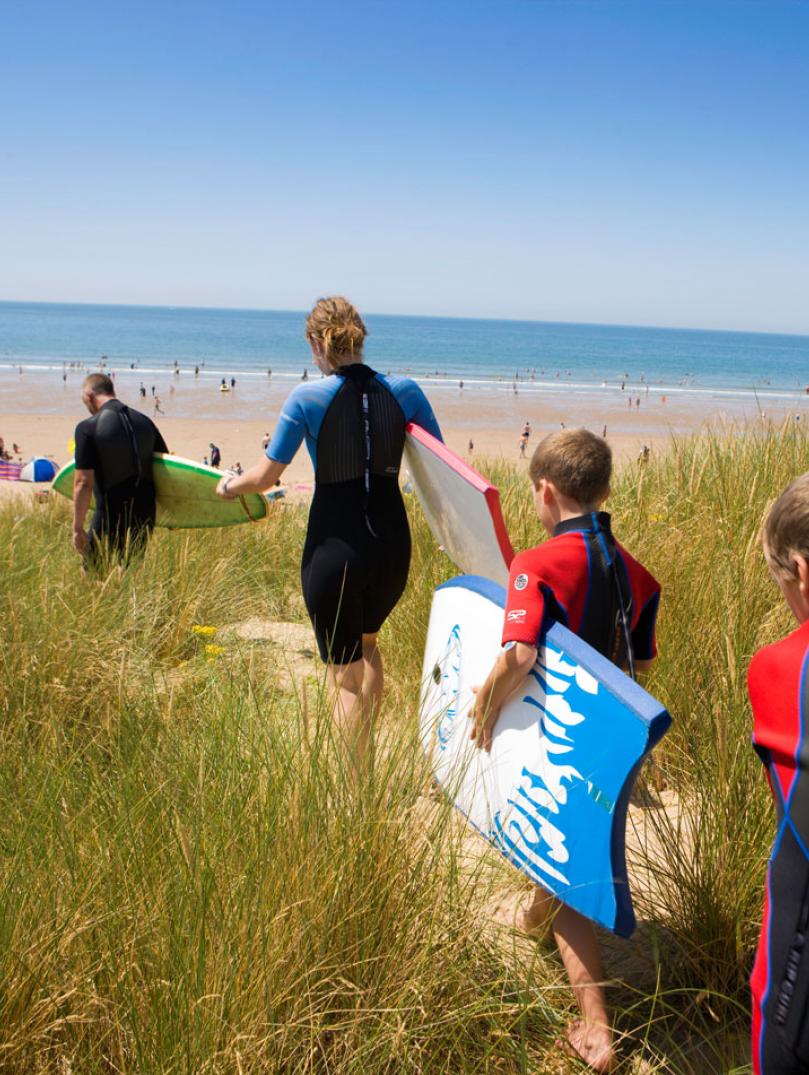 Family walking along sand dunes to the sea with surf boards