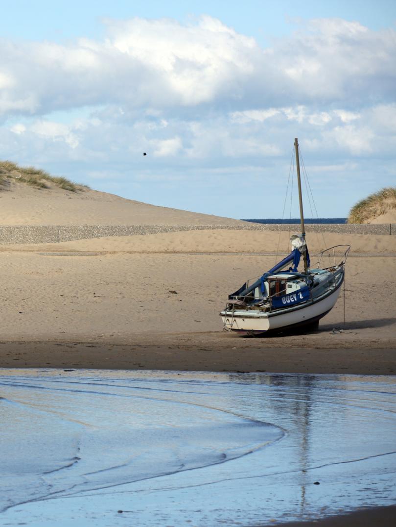Couple walking on Barmouth beach with a boat on the beach