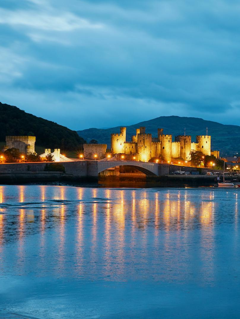 Conwy Castle lit up at night and reflection in water.