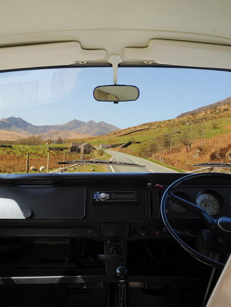 Innenansicht eines Campervans. Durch die Windschutzscheibe sieht man die Straße und die Landschaft von Snowdonia.