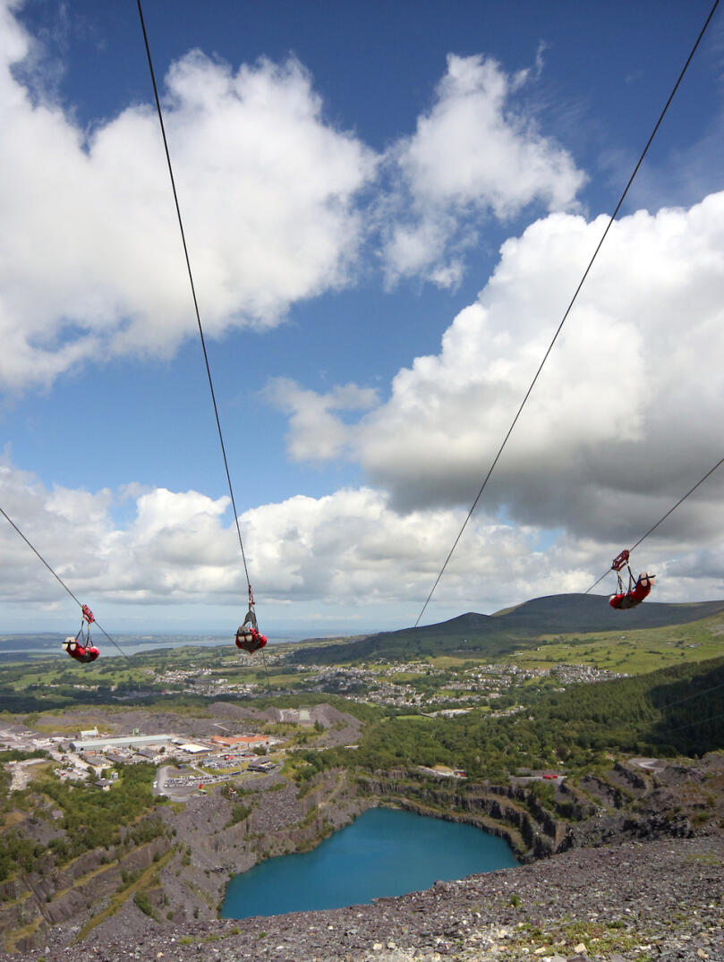Three people on four zip lines over a deep blue lake in a quarry.