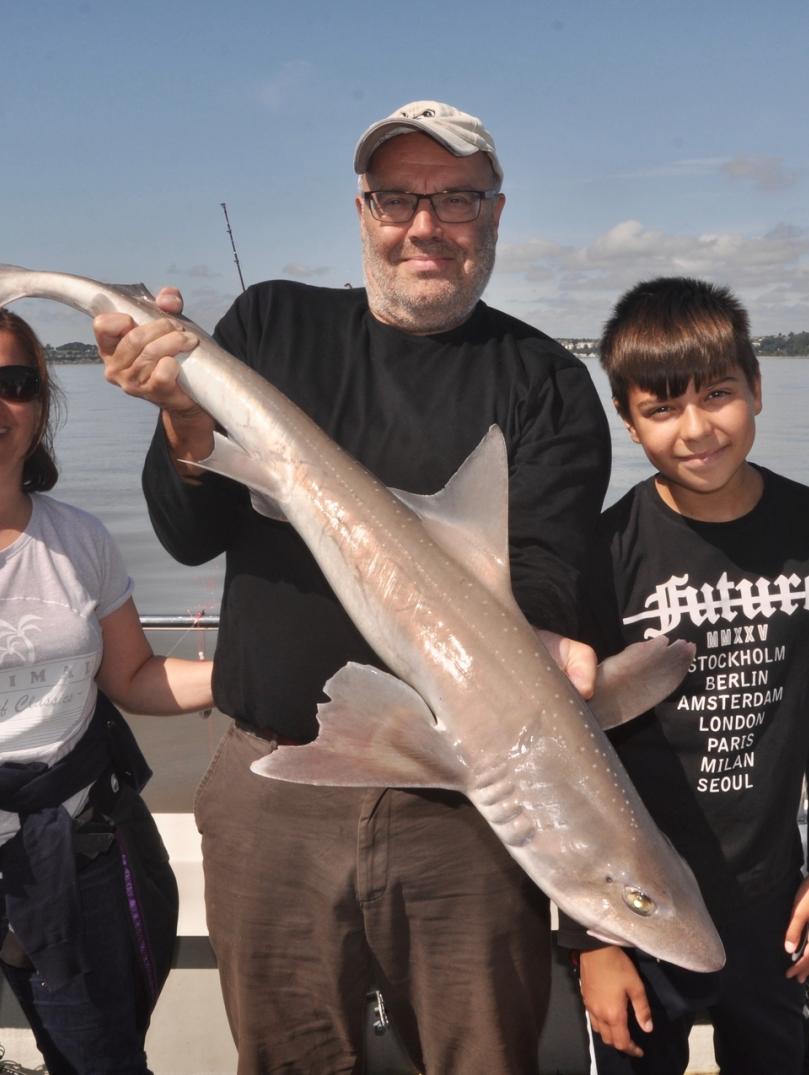 Two adults and a child on a boat hold up a 14lb starry smoothound fish.