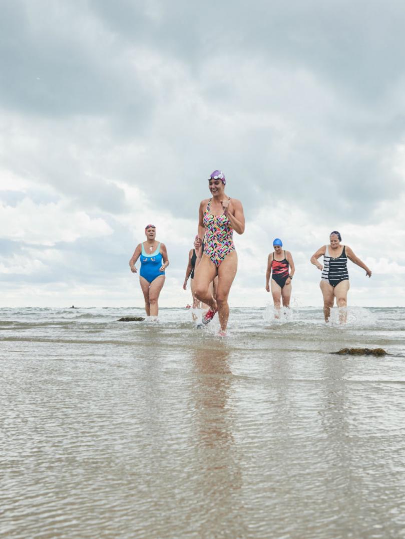 Women in swimming costumes running out of the sea towards the camera.