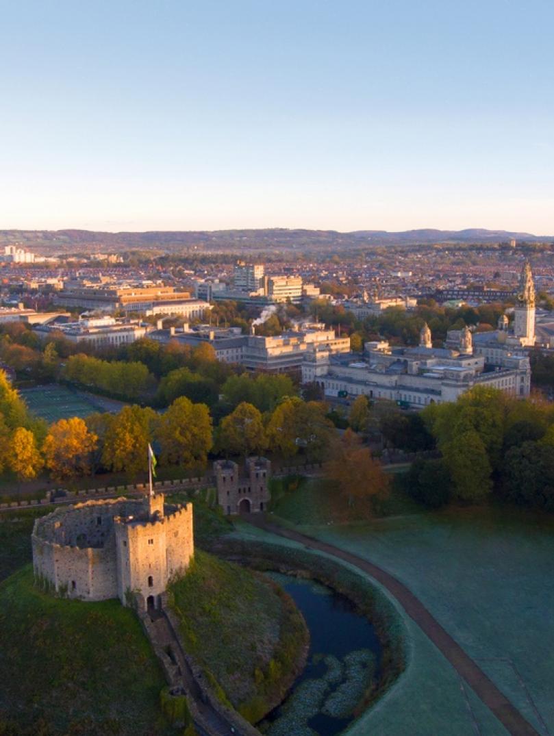 drone footage looking down onto Cardiff Castle with green grass and city view in far distance 