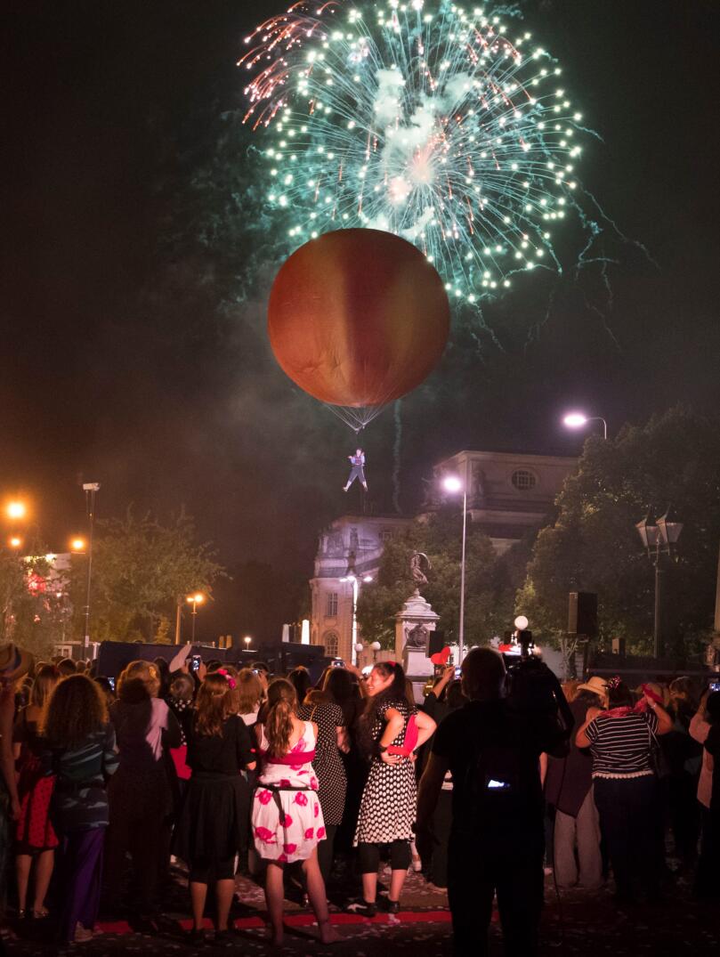 Menschenmenge beobachtet einen riesigen Pfirsich am Himmel vor einem Hintergrund von Feuerwerken