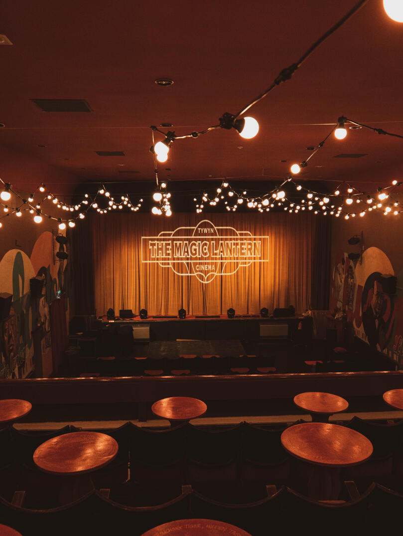 Inside the Magic Lantern cinema, with round wooden tables, cinema chairs and festoon lighting. 