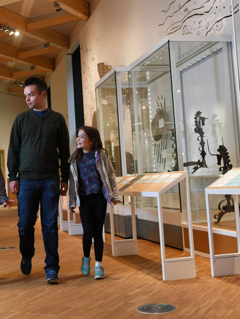 Eine dreiköpfige Familie beim Betrachten von Museumsvitrinen.