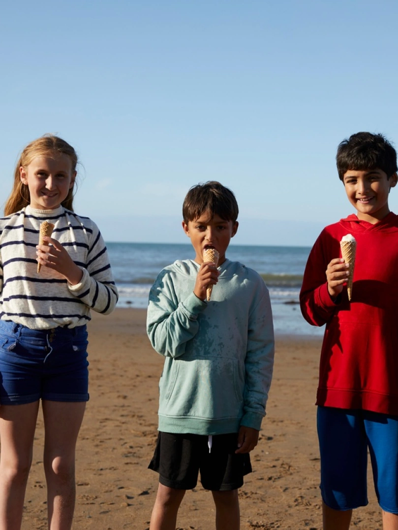 Three children standing on a beach on a sunny day eating ice cream 