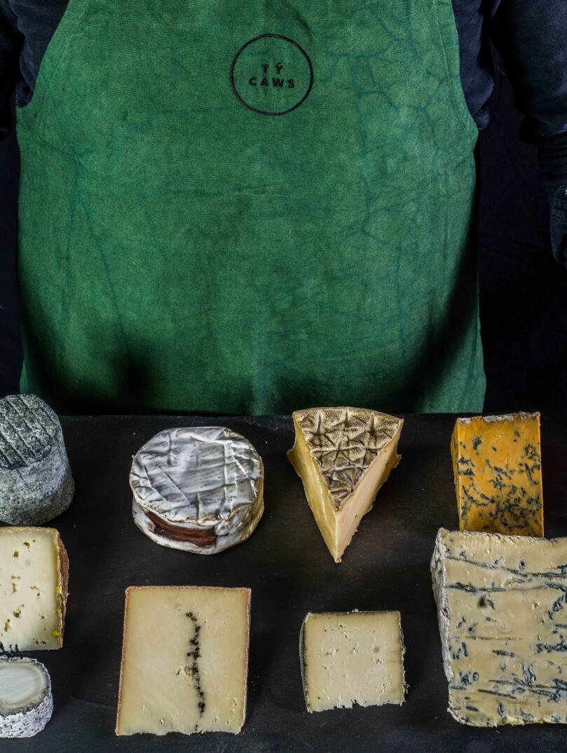 Ein Mann hält eine Schieferplatte mit neun verschiedenen Käsesorten darauf.