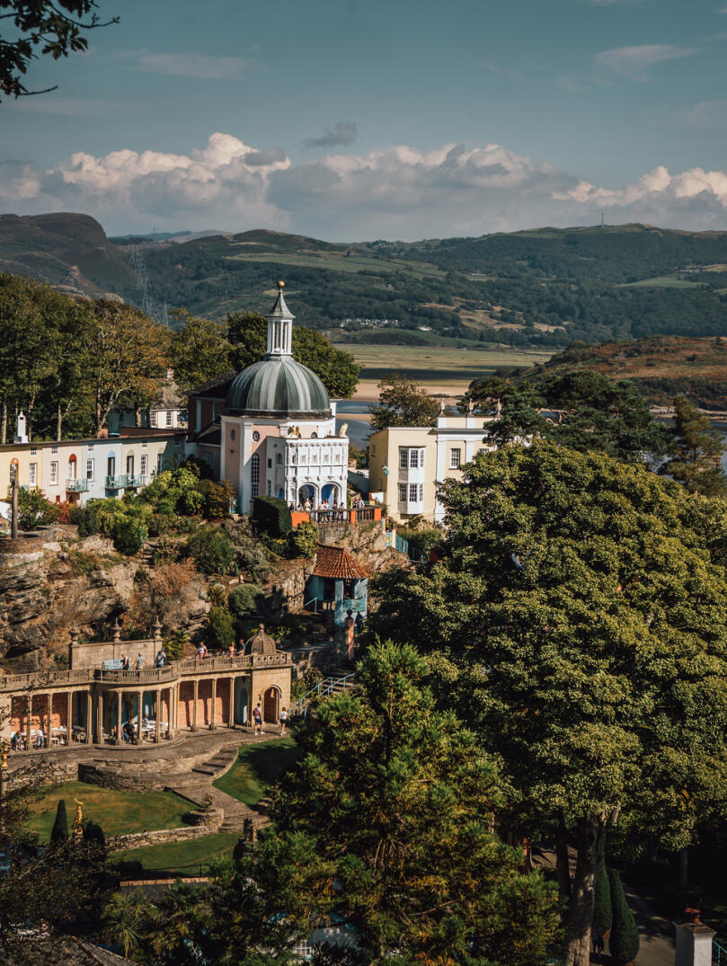 A view of the village of Portmeirion from above with the sea and mountains in the background.
