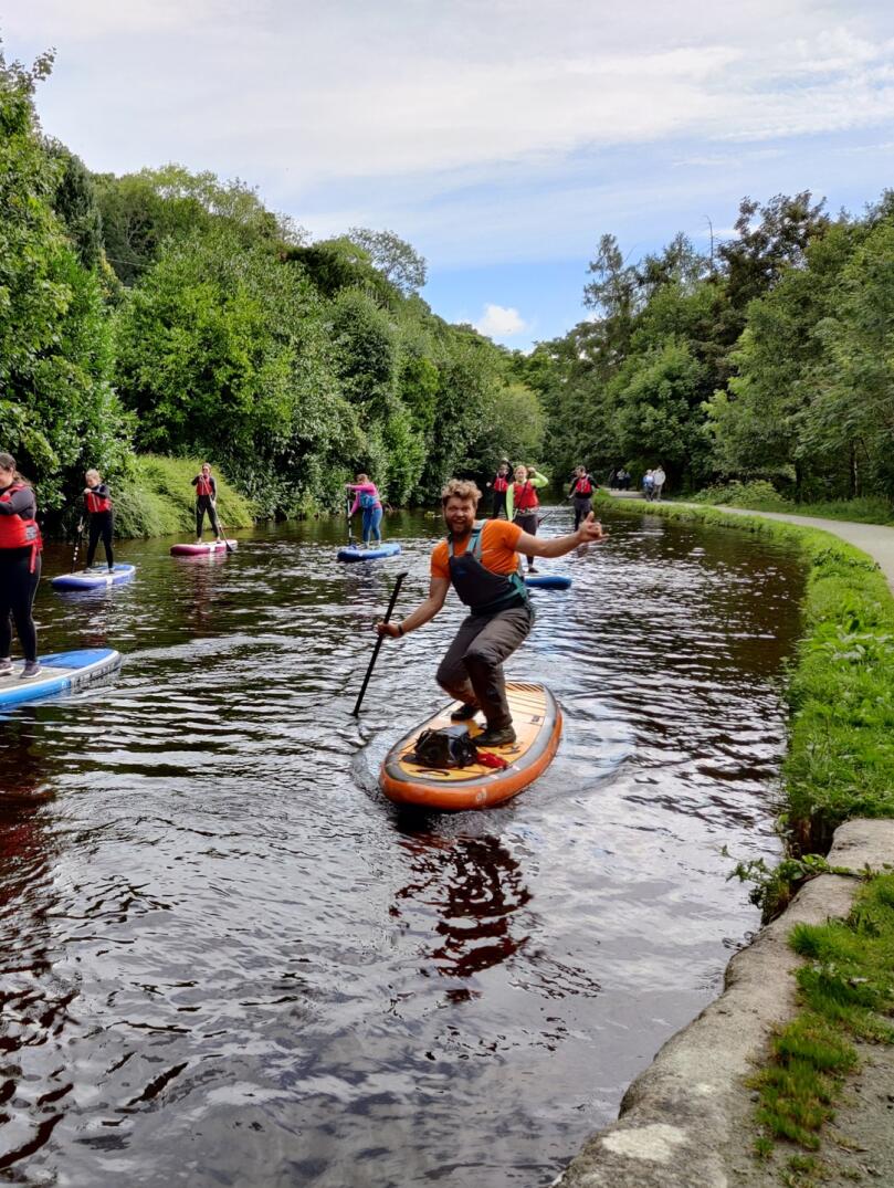 A group of people participating in stand up paddleboarding on a river.