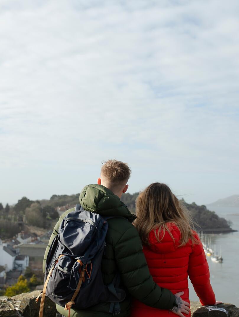 man and woman stood in castle with view of sea and boats.