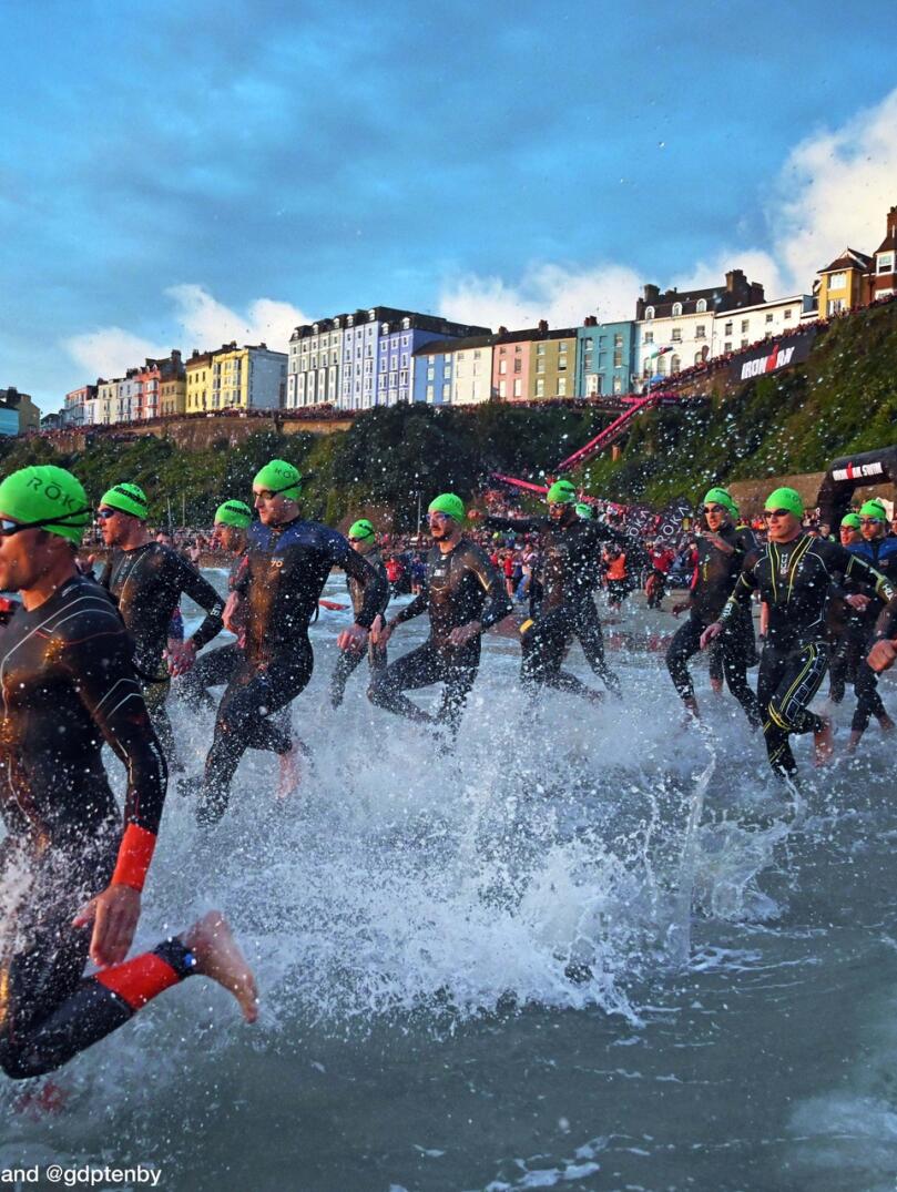 Many swimmers wearing green caps running into the sea.