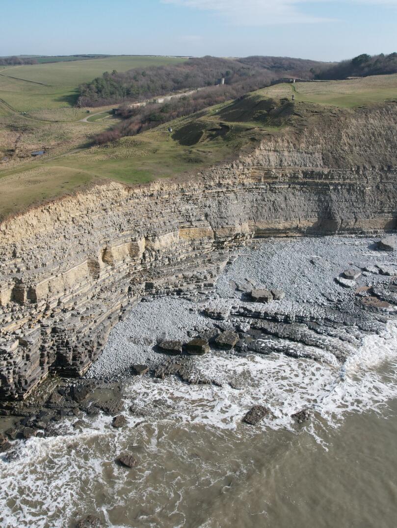 Aerial view of a limestone cliff edge over a pebbly beach.