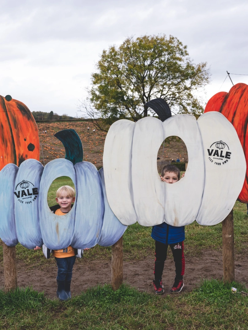 children inside pumpkin cut outs posing for photo.