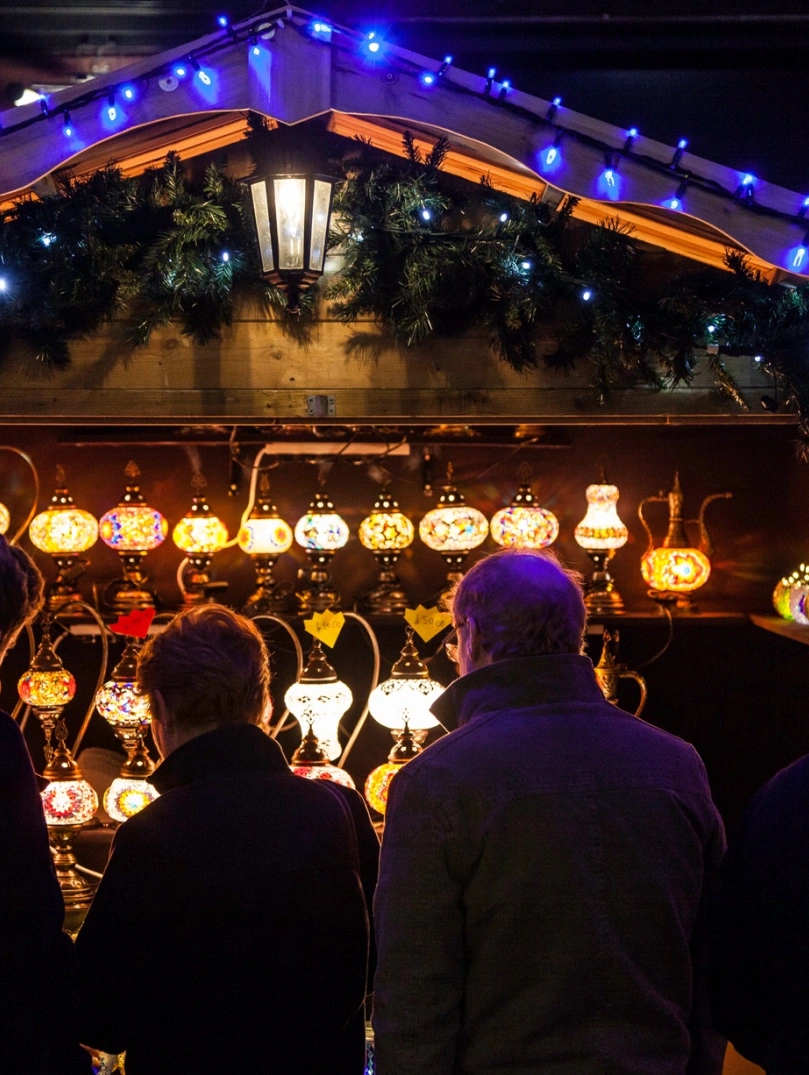 nighttime shot of Christmas market stall selling lamps with people in the foreground.