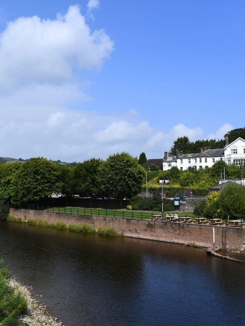 A large white hotel and castle overlooking a river, with a promenade alongside.