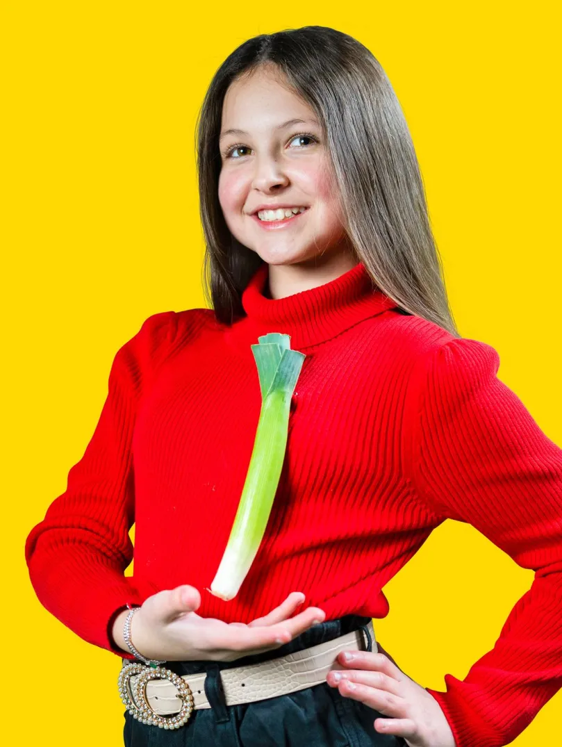 Merch ifanc mewn het draddodiadol Gymreig a siwmper goch yn dangos cenhinen wedi ei binio ar ei siwmper