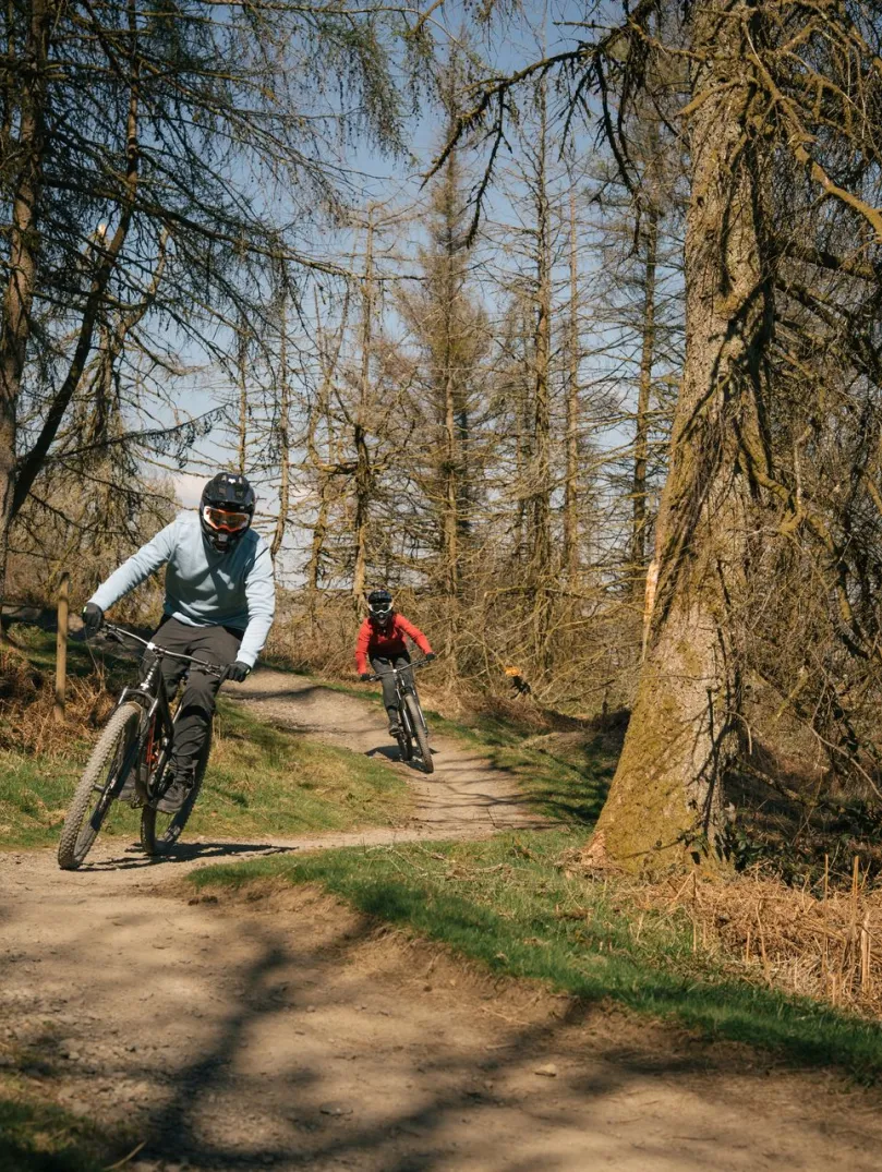 Two people mountain bikes on trail in bike park.