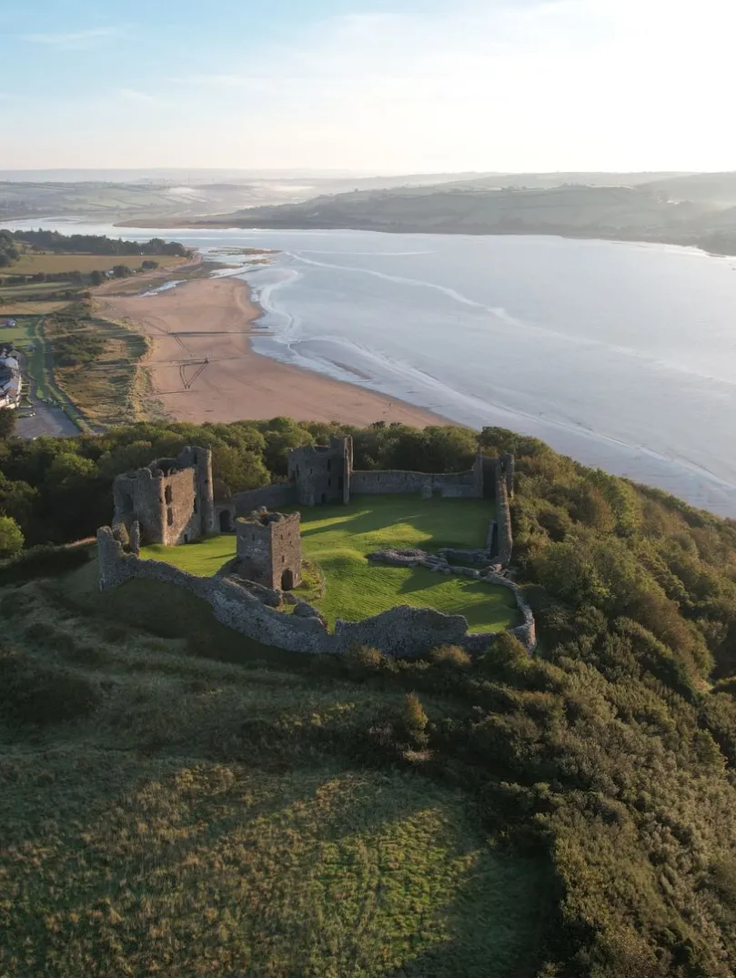 Aerial view of castle  high above coast with views of sea and countryside.