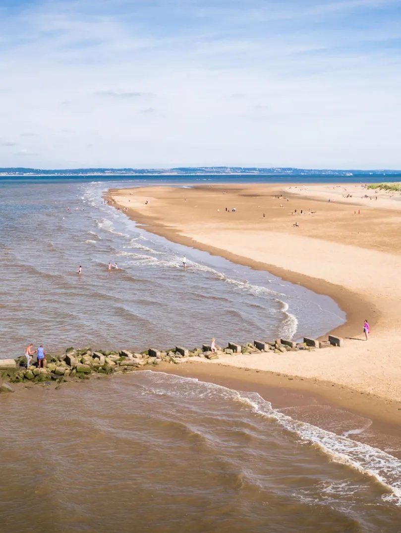A short, white-painted lighthouse on a beach backed by grassy dunes.
