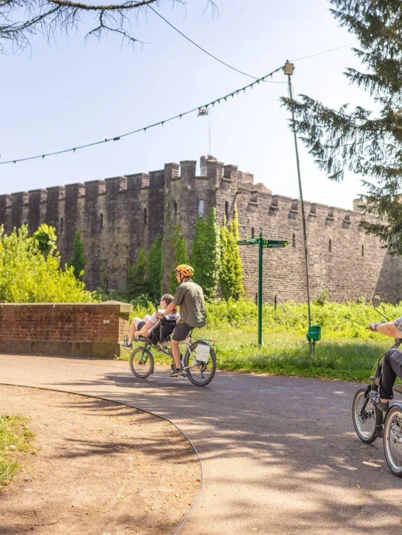 A family cycling in a city centre park with a castle in the background.