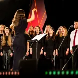 a choir singing with a conductor stood in front 