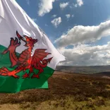 The Welsh dragon flag flying over a mountain landscape with blue sky.