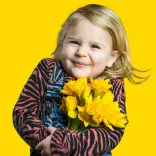 child smiling and holding a bunch of yellow daffodils