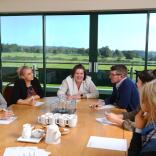 People around a meeting table with views of a racecourse beyond.