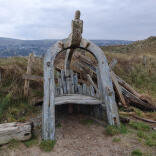 A wooden medieval chair on a walking trail with views of mountains beyond.