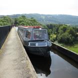 A narrowboat travelling along an aqueduct on a sunny day.