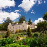 A cream coloured historic manor house surrounded by flower filled gardens