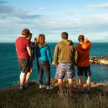 Eine Gruppe von Menschen auf einem Küstenpfad mit Blick auf die dahinter liegende Landschaft.