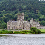 A castle in a parkland with a lake in the foreground.