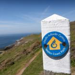 Ein weißer Pfosten mit einer blauen Plakette zeigt Wanderern den Weg auf dem Wales Coast Path.