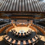 Chairs and tables set in a circle inf the debating chamber of a parliament building.