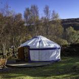 A white yurt with seating outside surrounded by trees at Graig Wen.
