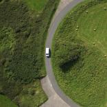 A white vehicle curving its way around a green field near Strumble Head, Pembrokeshire.