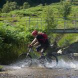 A mountain biker cutting through a river in Ceredigion. 