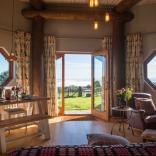 Inside a wooden eco-cabin, with patio doors opening out onto a green field. 