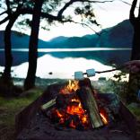Roasting marshmallows over the campfire infront of lake.