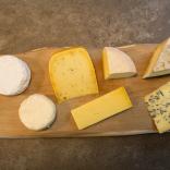 A selection of Welsh cheeses (Hafod Welsh Organic Cheddar, Teifi Cumin, Thelma’s Original Caerphilly cheese, Celtic Promise, Brefu Bach sheep’s milk cheese, Perl Las) on a wooden board.